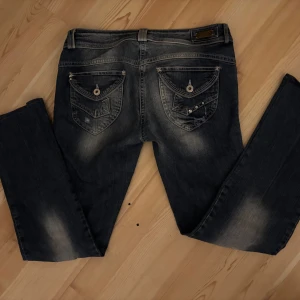 Mörkblå jeans med detaljer - Snygga mörkblå lågmidjade jeans med slitna detaljer och dekorativa knappar på bakfickorna. Den passar någon runt 160-165. Den är en flare passa form på mig. ”Kvarg” likna ande jeans 