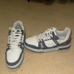 Louis Vuitton Sneakers - Stilrena och exklusiva! -  Säljer dessa snygga Louis Vuitton sneakers i marinblått och vitt. Perfekta för dig som älskar att kombinera lyx med komfort! De är i mycket gott skick och redo att bli en del av din garderob.
