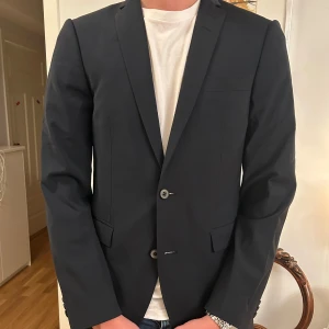 Svart kavaj från Tiger of Sweden - Snygg svart kavaj från Tiger of Sweden. Perfekt för både formella och semi-formella tillfällen. Kavajen har två knappar och klassiska fickor. En tidlös design som passar i många sammanhang.