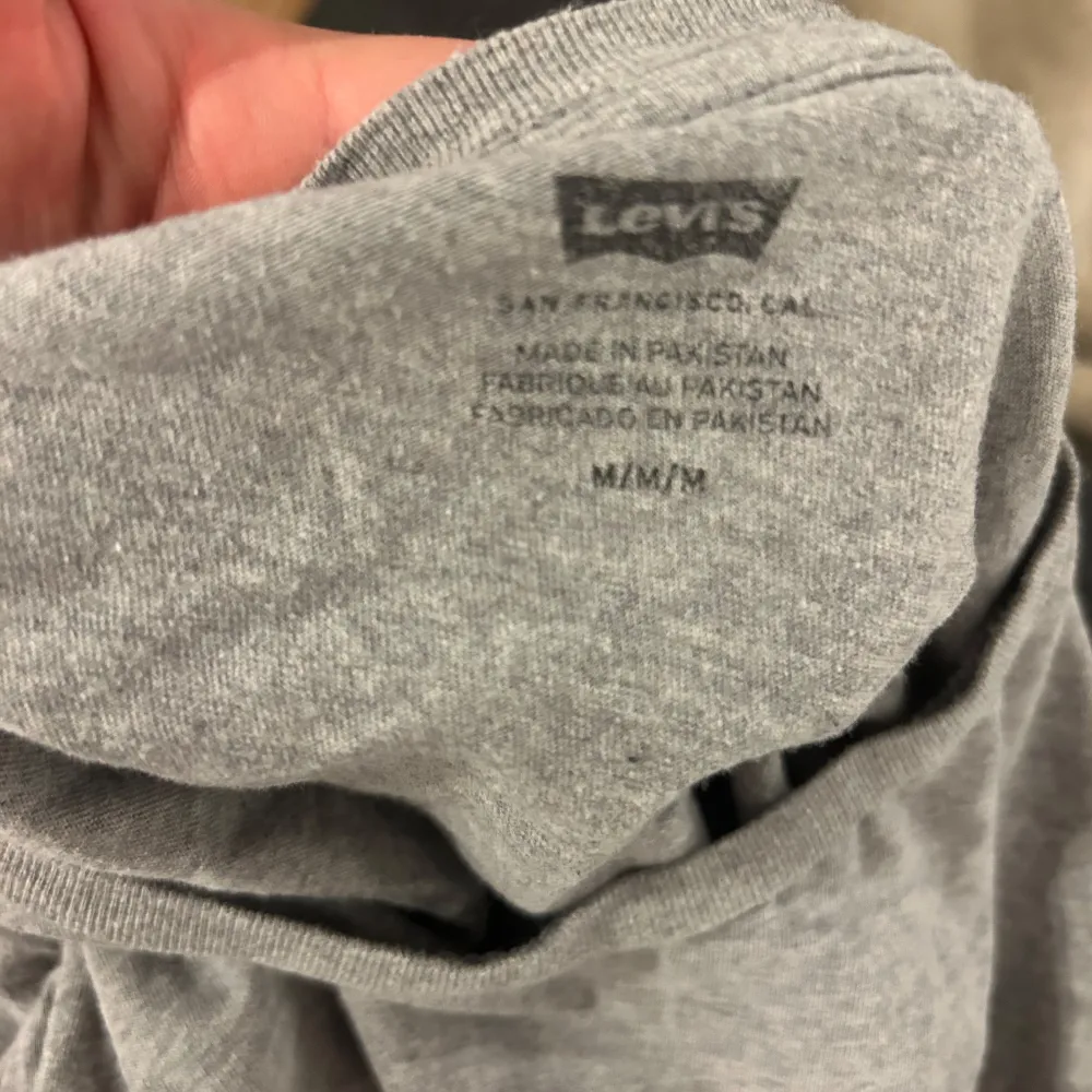 Säljer en grå t-shirt från Levi's med det klassiska röda logotyptrycket på framsidan. T-shirten är kortärmad och tillverkad i bomull, perfekt för en avslappnad stil.. T-paidat.
