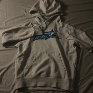 Vit hoodie från Lacoste - Säljer en vit hoodie från Lacoste med blått tryck på framsidan. Den har en känguruficka och justerbar huva. Perfekt för en avslappnad stil.de finns ett mini hål i ärmen med de går snabbt att fixa, den är för liten för mig så därför jag säljer denna😁