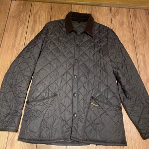 Brun quiltad jacka från Barbour - Säljer en stilren brun quiltad jacka från Barbour med knappar och krage i manchester. Perfekt för höst och vår med sin klassiska design och praktiska fickor. Ny pris 2199kr.