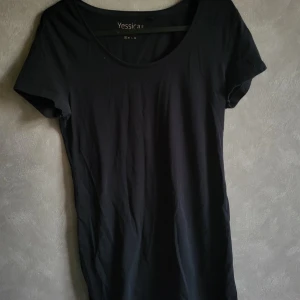 Svart t-shirt från Yessica - Säljer en enkel och stilren svart t-shirt från Yessica Basics. Perfekt för vardagsbruk med sin mjuka bomullskvalitet och bekväma passform. T-shirten har korta ärmar och rund halsringning.