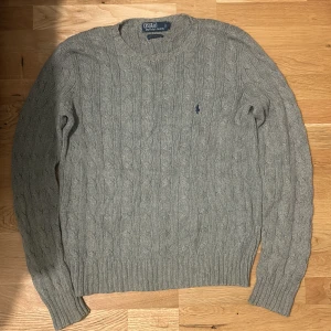 Ralph Lauren tröjor i  grå - En stilrena tröjor från Ralph Lauren i  grå. Den har kabelstickat mönster och den klassiska loggan på bröstet. Perfekta för en avslappnad och snygg look. för mer information eller bilder, kontakta mig.
