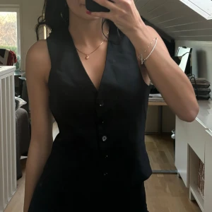 Svart väst med knappar - Snygg svart väst med knappar och v-ringad design. Perfekt för en stilren look.