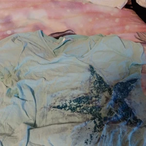 Ljusblå t-shirt med stjärnmönster - Säljer en ljusblå t-shirt från Bonprix med ett coolt stjärnmönster i mörkblått framtill. Perfekt för en avslappnad stil.