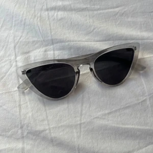 Transparenta cat-eye solglasögon - Snygga cat-eye solglasögon med transparent båge och mörka linser. Perfekta för en stilren look. Från Glitter. Oanvända