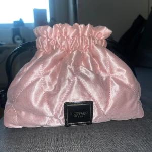 Rosa smink väska från Victoria's Secret - Söt rosa väska från Victoria's Secret. Väskan har en praktisk dragskoöppning och en elegant logotypdetalj framtill. 2 små fläckar på bild 4 som går att tvätta bort.