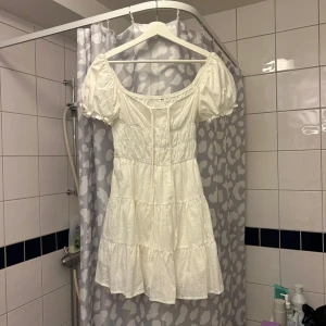 Vit klänning med puffärmar - Charmig vit klänning med puffiga kortärmar och en luftig passform. Klänningen har en söt volangdetalj och är perfekt för varma dagar.