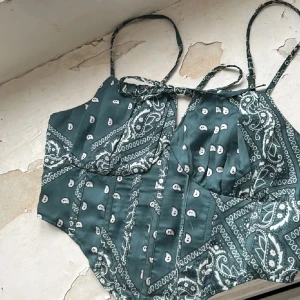 Grön mönstrad korsettopp - Snygg grön korsettopp med paisleymönster och smala axelband. Perfekt för en trendig look.