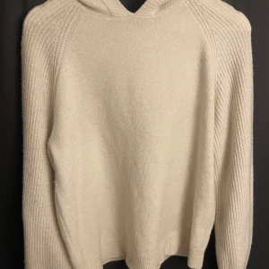 Vit stickad hoodie från Aware - Mysig vit stickad hoodie från Aware. Perfekt för kyliga dagar med sin mjuka och bekväma design. Tröjan har långa ärmar och en praktisk huva.