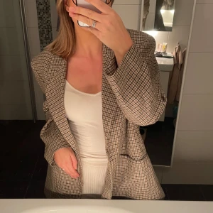 Rutig kavaj från Elena Mirò - Snygg rutig kavaj från Elena Mirò i ull. Kavajen har en klassisk passform med knappar framtill och är perfekt för en stilren look. Den har en tidlös design med jordnära färger som passar till många olika outfits.