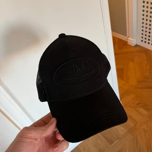 Svart keps från Von Dutch - Snygg svart keps från Von Dutch med meshdetaljer och justerbar baksida. Perfekt för en cool och avslappnad stil.