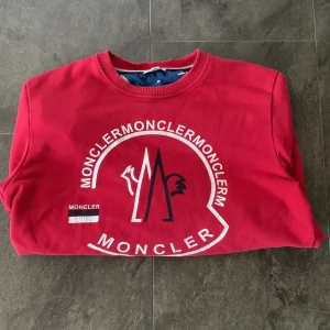 Röd sweatshirt från Moncler - Snygg röd sweatshirt från Moncler med stort tryck på framsidan. Tröjan har långa ärmar och rund halsringning. Perfekt för en avslappnad stil.