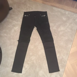 Svarta byxor från Balmain - Snygga svarta byxor från Balmain med dragkedjedetaljer och knappar framtill. Byxorna har en tight passform och är perfekta för en stilren look. De har också bakfickor med märkets logga.