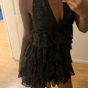 Svart glittrig klänning - Snygg svart klänning med glittriga detaljer och volanger. Den har en djup v-ringning och är ärmlös, perfekt för en festlig kväll 💕