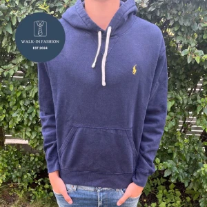 Mörkblå hoodie från Ralph Lauren - Säljer en snygg mörkblå hoodie från Ralph Lauren med den klassiska loggan broderad i gult på bröstet. Tröjan har en känguruficka och justerbar huva med vita snören. Perfekt för en avslappnad stil! Nypris 2300kr.  Obs: lånad bild. 