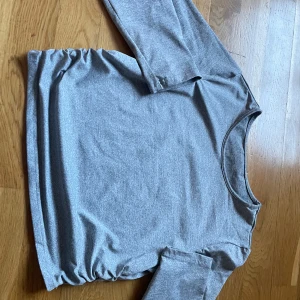 Grå långärmad topp med rynkdetalj - Snygg grå långärmad topp med unik rynkdetalj på sidan. Perfekt för en stilren och bekväm look. Tillverkad i mjukt material som känns skönt mot huden.