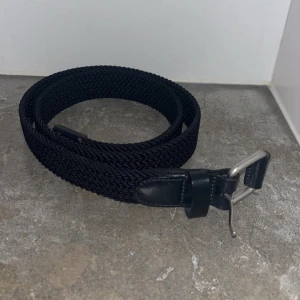 Arket Mörkblått flätat bälte med silverfärgat spänne - Snyggt svart flätat bälte med ett stilrent silverfärgat spänne. Perfekt för att ge en extra touch till din outfit. Bältet har svarta skinnliknande detaljer vid spännet.