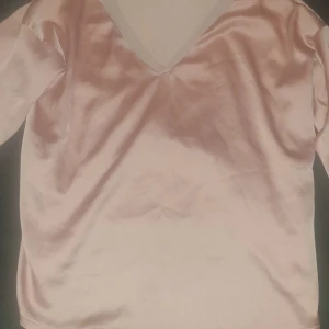 Rosa långärmad topp från Zara - Säljer en stilren rosa långärmad topp från Zara i ett mjukt och glansigt material. Toppen har en v-ringad design som ger en finare touch.