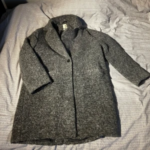 Grå kappa från H&M - Säljer en stilren grå kappa från H&M i ullblandning. Kappan har en klassisk design med knappar framtill och långa ärmar. Perfekt för kyligare vår/höstdagar och ger en elegant touch till din outfit. Jag är 170cm lång, och denna är i storlek S.