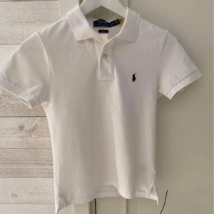 Vit pikétröja från Ralph Lauren - Säljer en klassisk vit pikétröja från Ralph Lauren i slim fit. Tröjan har korta ärmar och en broderad logotyp på bröstet. Perfekt för en stilren look.