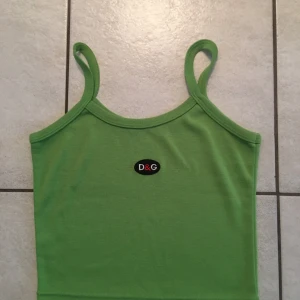 Grön linnetopp från D&G - Snygg grön linnetopp från D&G med smala axelband och en liten logga på bröstet. Perfekt för varma dagar eller som ett lager under en jacka. Enkel och stilren design som passar till många olika outfits.