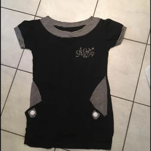 Svart och randig klänning - Snygg svart klänning med randiga detaljer och korta ärmar. Klänningen har en dekorativ logga på bröstet och praktiska fickor framtill. Perfekt för en avslappnad stil.