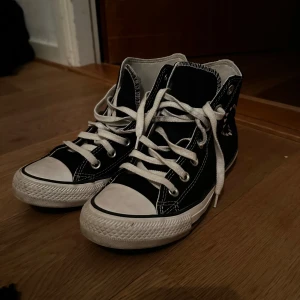 Svarta Converse Chuck Taylor All Star - Snygga svarta Converse Chuck Taylor All Star med vita snören och detaljer. Skorna har ett hjärtmönster och texten 'love' broderad på sidan.