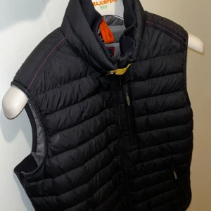 Svart dunväst från Parajumpers M  - Säljer en snygg svart dunväst från Parajumpers med dragkedja och hög krage. Perfekt för kyliga dagar och har en stilren design. Västen är quiltad och har en praktisk ficka med dragkedja.