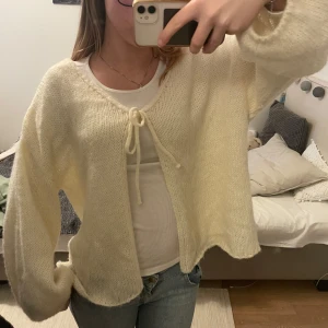  stickad kofta med knytband - Stickad kofta som man kan knyta till en rosett, gul/cremevit färg 