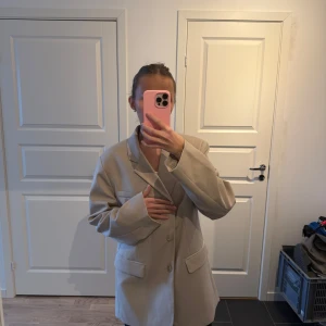 Beige kavaj - Säljer en stilren beige kavaj med en klassisk design. Kavajen har en oversize passform med långa ärmar och knappar framtill. Perfekt för en chic och elegant look.