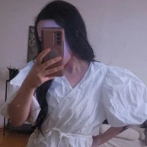 Vit omlottblus med puffärmar - Säljer en stilren vit omlottblus med puffiga kortärmar och knytband i midjan. Perfekt för en elegant och luftig look.