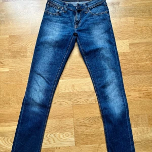 Blå jeans från Nudie - Snygga blå jeans från Nudie i modellen Tight Long John. De har en slim passform och är tillverkade i en bomullsblandning med lite stretch för extra komfort. Perfekta för en stilren look.