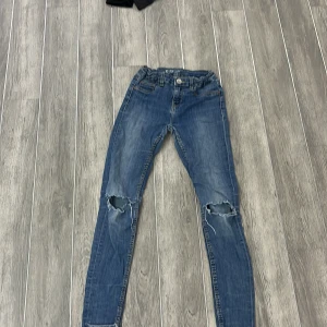 Blå skinny jeans med slitningar - Snygga blå skinny jeans med slitningar på knäna. De har en klassisk femficksdesign och knappgylf. Perfekta för en avslappnad stil.
