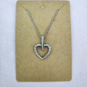 Halsband med hjärta och strass - Elegant halsband med ett hjärta dekorerat med glittrande strass. Kedjan är i silverfärg och hjärtat hänger från en stilren stav. Perfekt för att ge en gnistrande touch till din outfit. Äkta silver.