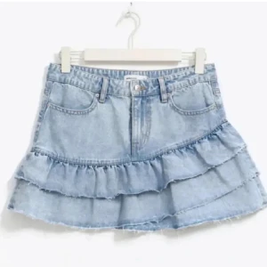 Jeanskjol med volanger från Gina tricot - Snygg jeanskjol i ljusblå denim med volangdetaljer. Kjolen har en kort längd och och dragkedja framtill. Knappt använd men kom med bud 💕