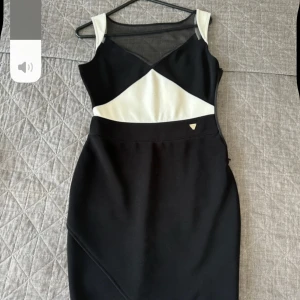 Svart och vit klänning från Guess - Snygg svart och vit klänning från Guess med ett stilrent mönster. Klänningen har en v-ringad design och är ärmlös med en dragkedja på sidan. Perfekt för en chic look!