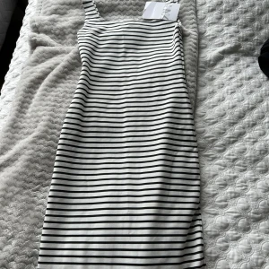 Randig klänning - Snygg och stilren randig klänning i svart och vitt. Klänningen har en tight passform och är ärmlös, vilket gör den perfekt för varmare dagar. Den är knälång och har en slits på baksidan längst ner. Aldrig använd. 