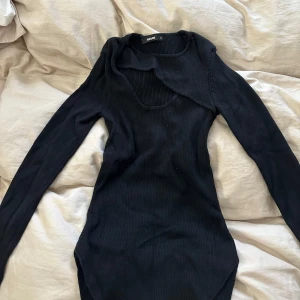 Svart långärmad med urringning - En svart långärmad tröja från bikbok med en öppen detalj på bröstet. Sitter tight hela vägen och har en liten slits längst ner på sidorna. Väldigt bra skick då den endast är använd ca 2-3 gånger. Normal i storlek