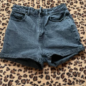 Svarta jeansshorts - Snygga svarta jeansshorts med hög midja och klassisk femficksdesign. Perfekta för en avslappnad stil. De har en dragkedja framtill och uppvikta benslut för en trendig look.