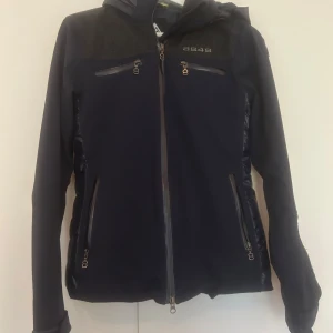 Mörkblå jacka från 8848 Altitude - Snygg mörkblå jacka från 8848 Altitude med dragkedja och flera praktiska fickor. Jackan har en mix av material med quiltade detaljer på sidorna och axlarna. Jackan har ett snölås.