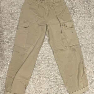 Beige cargobyxor från Carhartt - Säljer ett par beige cargobyxor från Carhartt med avslappnad passform. Byxorna har flera praktiska fickor och knappar, perfekt för en casual look. De är tillverkade i slitstarkt material och har en klassisk design. Perfekt för en skön och stilig skateboard dag, Nypris 1100kr