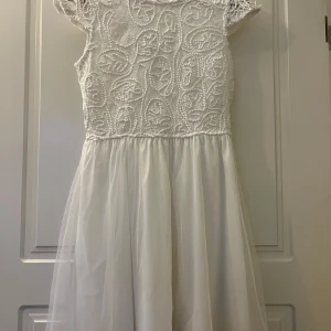 Vit spetsklänning med broderad topp - Charmig vit klänning med en vacker broderad spets på toppen och en luftig kjol. Klänningen har korta ärmar och en djup v-ringad rygg. Perfekt för sommarens speciella tillfällen. Studenten kanske. Inköpt från Bubbleroom till Student men blev fel storlek, Aldrig andvänd. Storlek 38