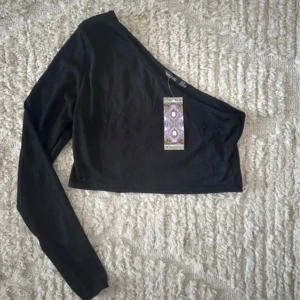 Svart oneshoulder topp från Boohoo - Snygg svart oneshoulder topp från Boohoo. Toppen är croppad och gjord i ett mjukt material som ger en bekväm passform. Oanvänd med etikett kvar 