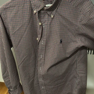 Rutig skjorta från Ralph Lauren - Snygg rutig skjorta från Ralph Lauren i rött, blått och vitt. Skjortan har en klassisk krage med knappar och broderad logga på bröstet. Perfekt för en stilren look! Den är endast använd tre gånger behövs bara strykas pris kan diskuteras 