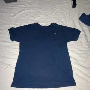 Mörkblå t-shirt från Tommy Hilfiger - Säljer en klassisk mörkblå t-shirt från Tommy Hilfiger. Den har en liten logga på bröstet och är tillverkad i ett mjukt material. Perfekt för en avslappnad stil.