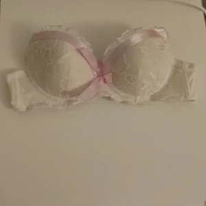 Vit spets-bh med rosa rosett - Elegant vit bh i spets med en söt rosa rosett framtill. Perfekt för att känna sig extra fin under kläderna.