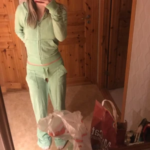 Grön mjukisbyxa och hoodie från Juicy Couture - Säljer ett set med grön mjukisbyxa och matchande hoodie från Juicy Couture. Byxorna har en bekväm passform med snörning i midjan och hoodien har dragkedja och huva. Perfekt för en avslappnad stil.