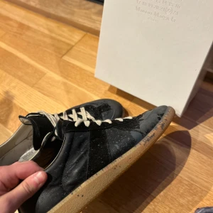 Maison Margiela - Snygga svarta sneakers från Maison Margiela med vita snören och en gummisula. Skorna har en stilren design med en touch av elegans, perfekt för den modemedvetna. Levereras med originalförpackning. Tröttnat på mina skor original box medföljer dust bags finns, sånt legit check kort oxå. Hör av dig vid eventuella frågor 😊mvh Leo 